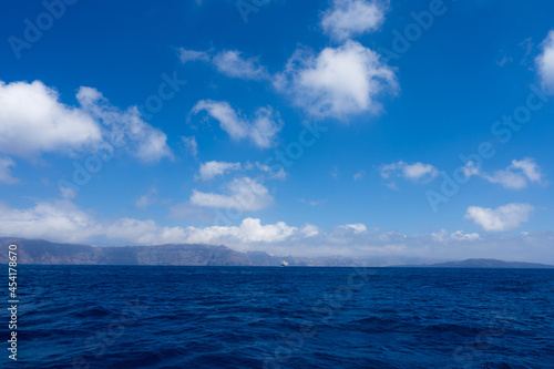 View from sea of silhouette of Santorini island, Greece. Luxury tourism. Blue cloudy sky.