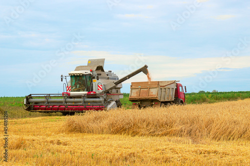 Harvester combine harvesting wheat and pouring it into dump truck during wheat harvest at the end of summer. Concept of a rich harvest. Farming agricultural background.