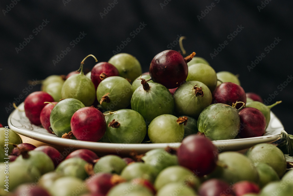 Gooseberry. Green and red gooseberry berries on a black background. Gooseberries on a white plate on a black background Gooseberry. Green and red gooseberry berries on a black background. Gooseberries on a white plate on a black background