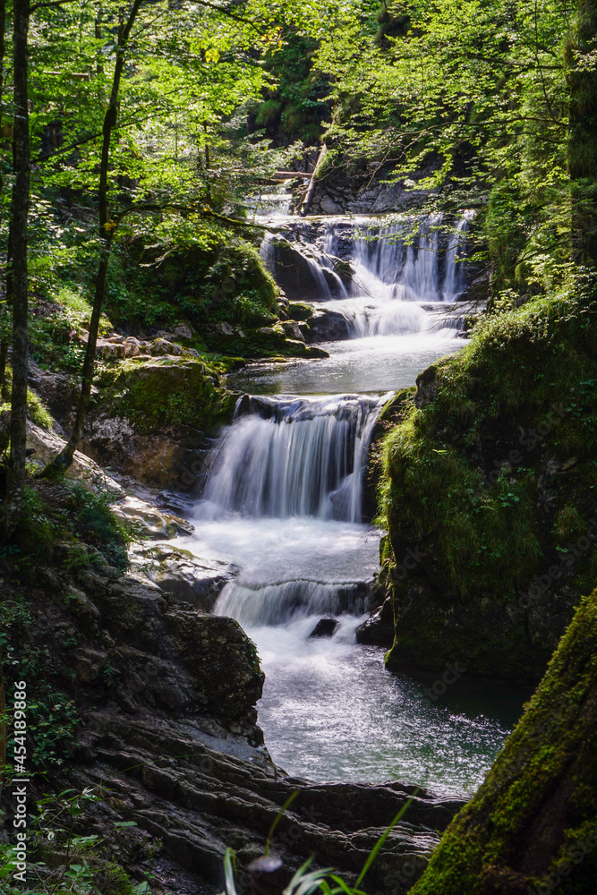 Ein Wasserfall mitten im Wald. In mehreren Stufen fließt das Wasser in einen Fluss.
