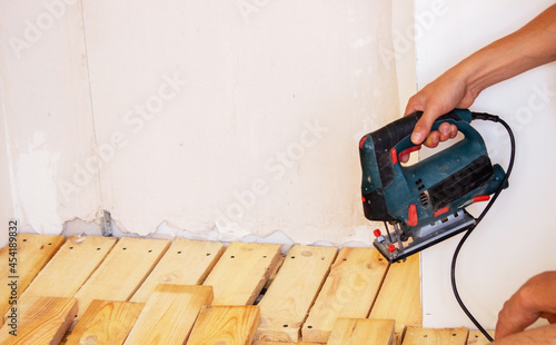 A man cuts a board with an electric saw. Repair of the floor in the house. Selective focus.