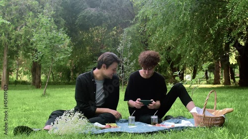 The guy plays the game on the phone, and the second watches the process in nature in the summer