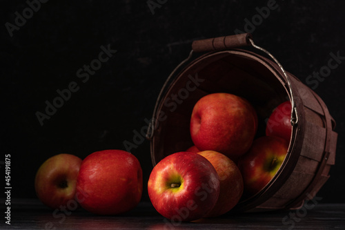 Dark and moody view of apples spilling from a bucket on dark color table and background