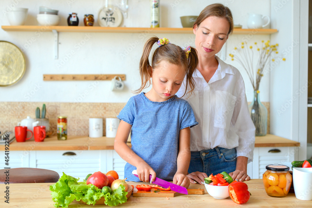 Happy mom teaches little daughter to cook healthy food, mom and girl talking, smiling, doing useful activities in the kitchen