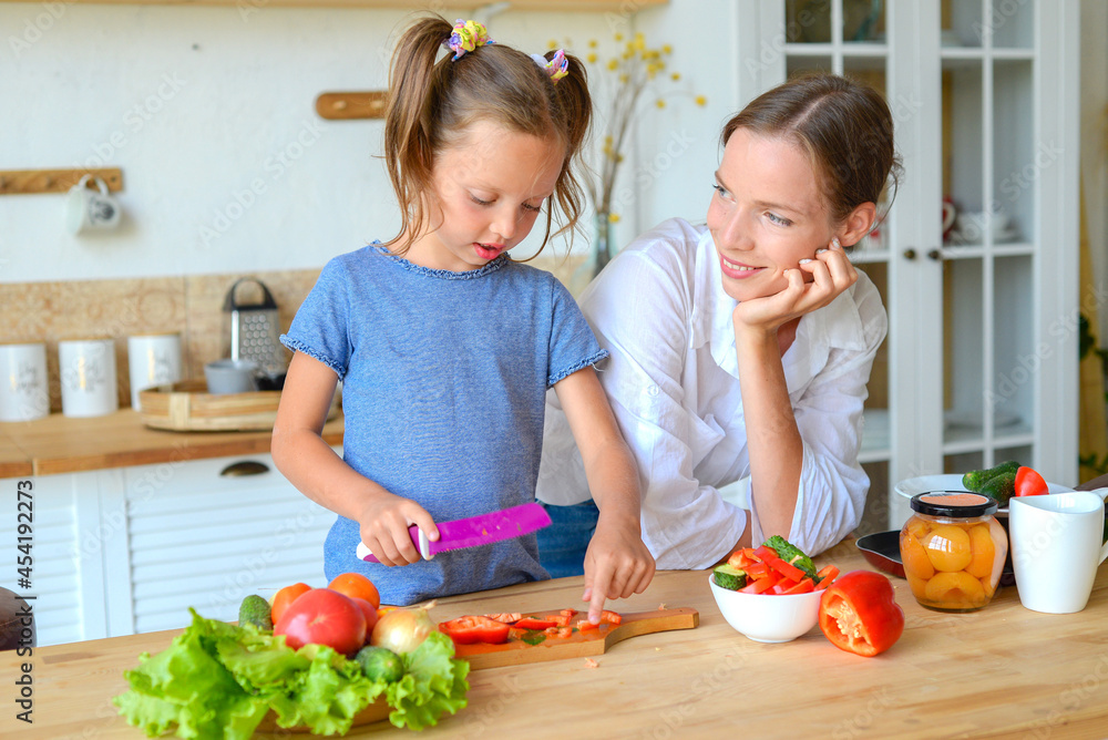 Happy mom teaches little daughter to cook healthy food, mom and girl talking, smiling, doing useful activities in the kitchen Happy mom teaches little daughter to cook healthy food, mom and girl talking, smiling, doing useful activities in the kitchen