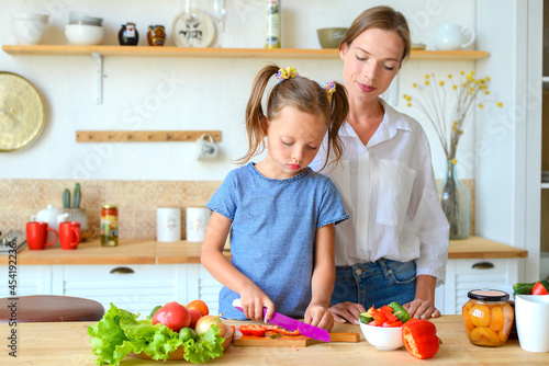 Happy mom teaches little daughter to cook healthy food  mom and girl talking  smiling  doing useful activities in the kitchen