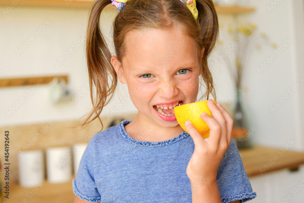 Little smiling cute blonde girl in blue t-shirt holding fresh lemon halves, showing tongue and feeling sour. Healthy lifestyle and clean food concept Little smiling cute blonde girl in blue t-shirt holding fresh lemon halves, showing tongue and feeling sour. Healthy lifestyle and clean food concept