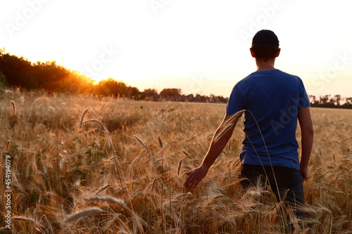 man walks through a wheat field at sunset