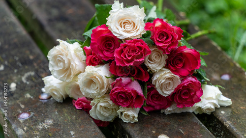 Bouquet of roses  white and pink  abandoned on a wooden bench  in the middle of a park  on a rainy day  close up 