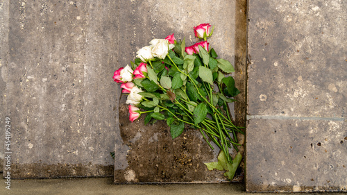 Bouquet of roses, white and pink, placed on the steps of stone stairs, covered with rain, outside