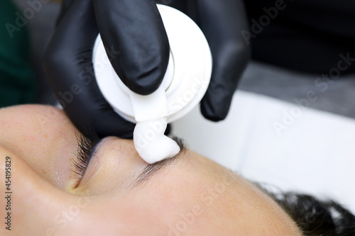 the master applies a moisturizing foam to the model's eyebrow before the lamination procedure