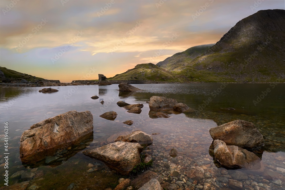 The sun rising over Levers Water above the Coniston Copper Mines valley in Cumbria, shot in landscape with large rocks in the foreground