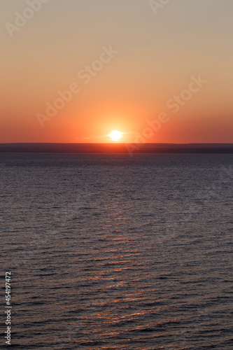 Beautiful colorful sunset over the sea. The red sun and the absence of clouds. Sea horizon. Aerial view. Landscape. The concept of a postcard picture. Light waves on the sea surface