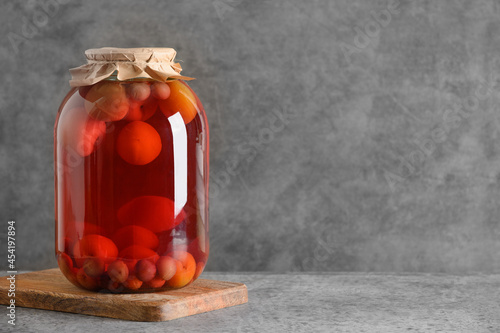 Homemade canned fruits plum and cherry compote in large glass jars on gray table. Copy space. photo