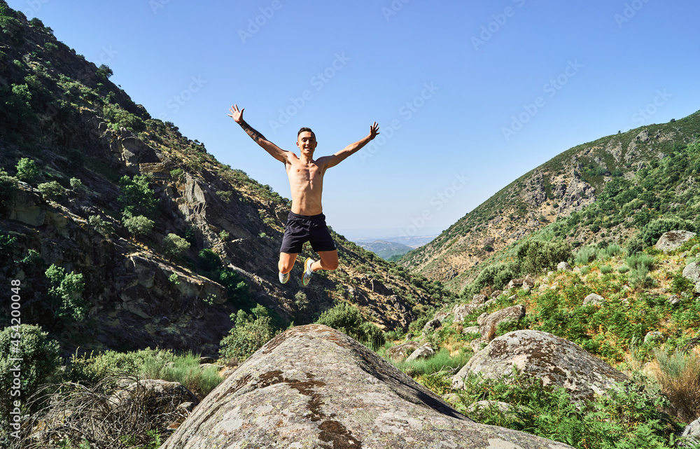 Obraz premium Young caucasian man, free and happy, jumping with open arms in a beautiful landscape with mountains