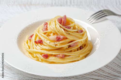 Spaghetti carbonara in a white plate. Spaghetti, pancetta and sauce made of egg yolk and parmesan cheese, black pepper. Close-up.