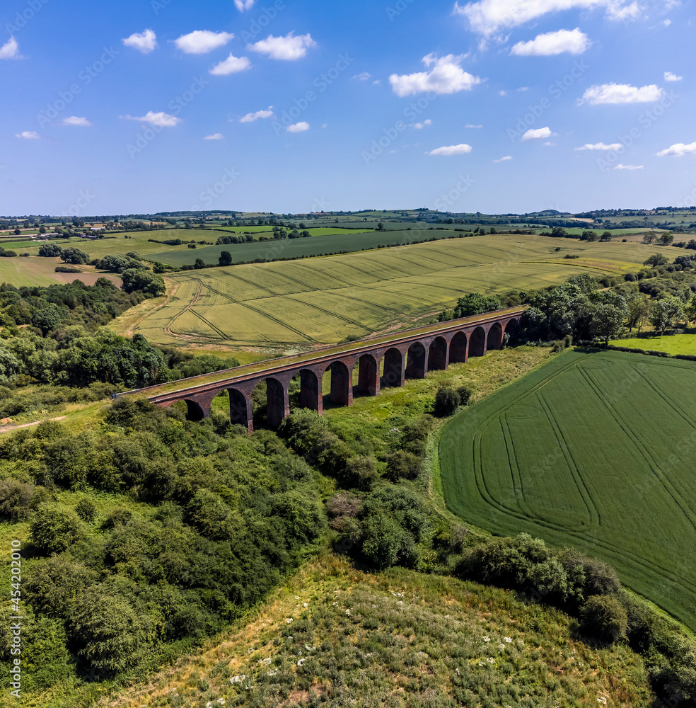 An aerial view across countrydside and the Victorian railway viaduct at John O'Gaunt valley, Leicestershire, UK in summertime