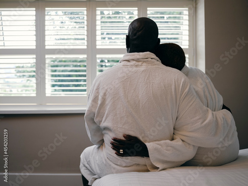 UK, Rear view of mature couple in bathrobes sitting on bed in hotel room