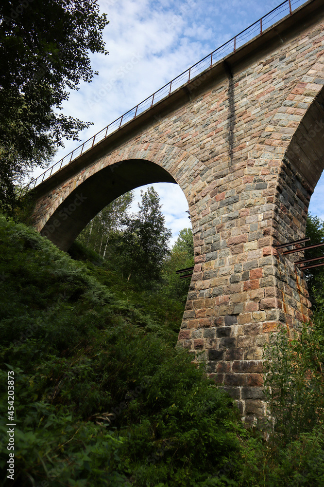 old abandoned stone railway arch bridge over the river in the forest