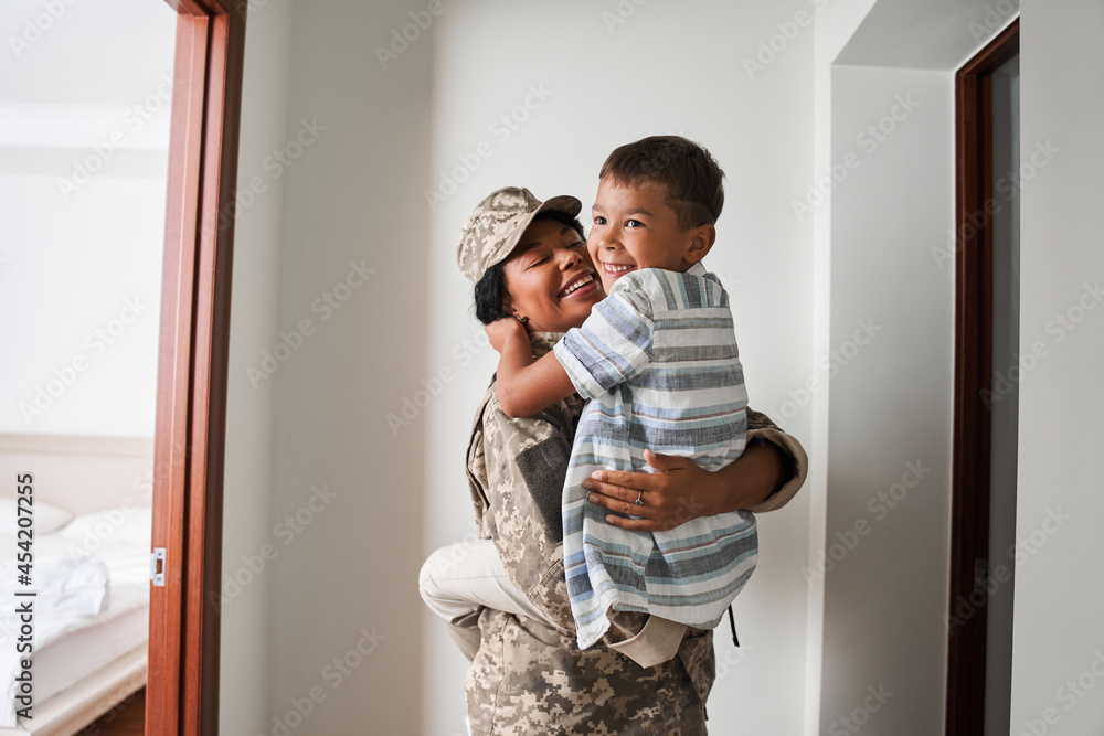 Black female soldier holds son on arms after army - obrazy, fototapety, plakaty 
