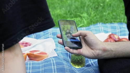 A man's hand holds a phone and flips through photos in nature in the summer