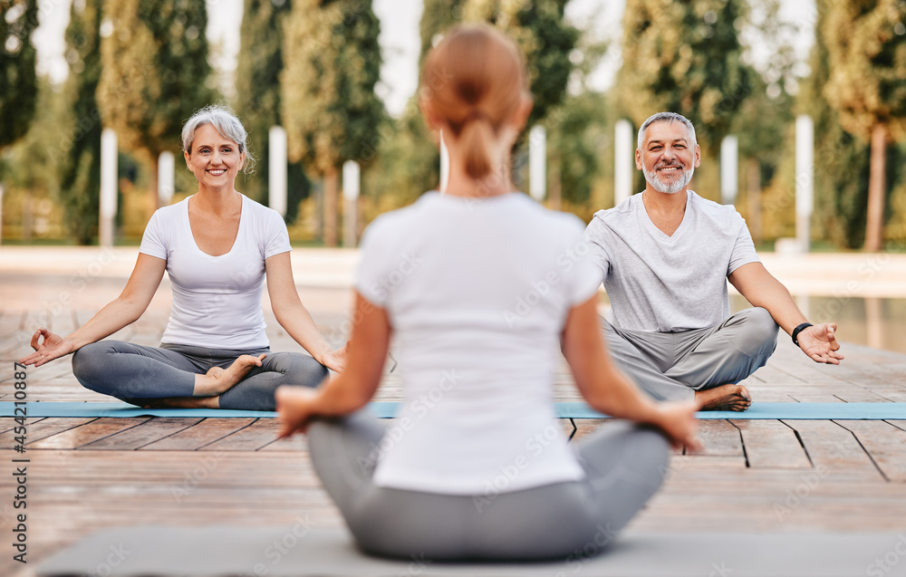 Senior couple staying in lotus pose in front of female yoga trainer during yoga class in city park