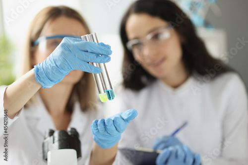 Woman scientist chemist showing test tubes with blue and yellow liquid in laboratory closeup