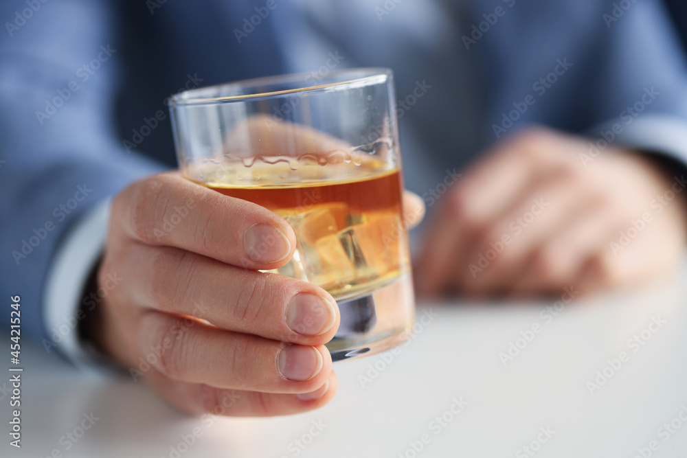 Man in suit holding glass of whiskey with ice in his hand closeup Man in suit holding glass of whiskey with ice in his hand closeup