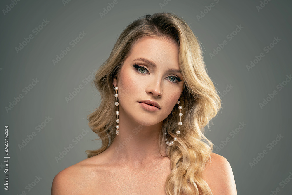 Fashion beauty portrait of young caucasian woman with pearls jewelry and elegant hairstyle. Blonde girl with long wavy hair.