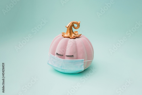 Pink halloween pumpkin with golden petiole and eyelashes and surgical face mask. Green mint background color. Minimal design.