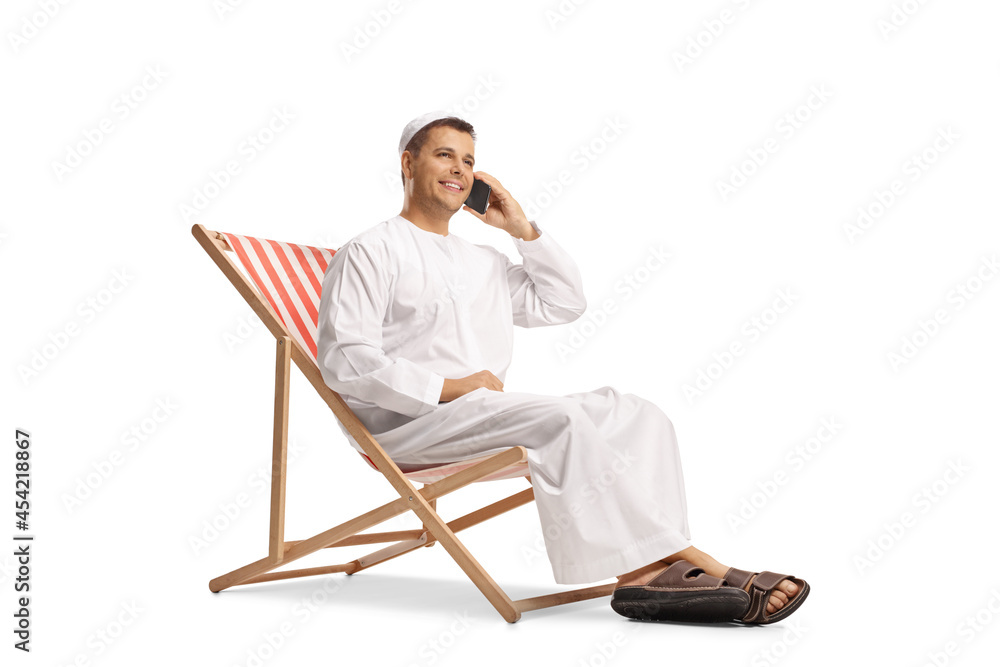 Young man in ethnic clothes sitting in a beach chair and making a phone call