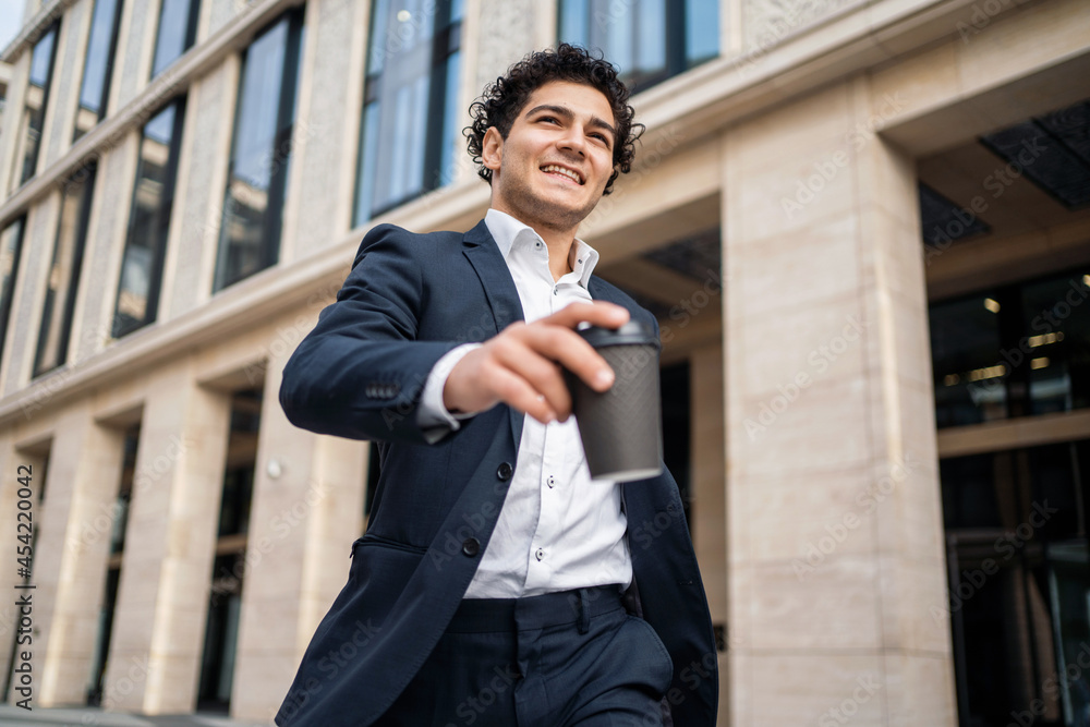 A young businessman holds a cup of coffee in his hand. A male entrepreneur goes to work. The financier is in a good mood and a modern business suit. A young businessman holds a cup of coffee in his hand. A male entrepreneur goes to work. The financier is in a good mood and a modern business suit.