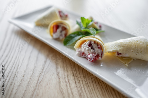 thin pancake rolls with cottage cream cheese and strawberry on wooden background