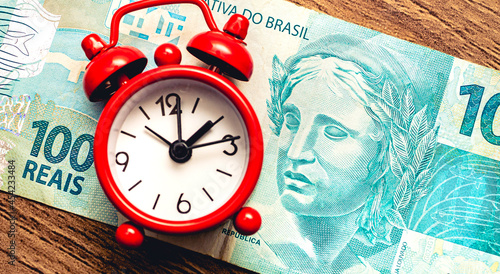 Real - BRL, dinheiro do Brasil. Um pequeno relógio despertador de cor vermelha sobre cédulas de Real Brasileiro. Conceito de aposentadoria, planejamento financeiro e investimentos. photo