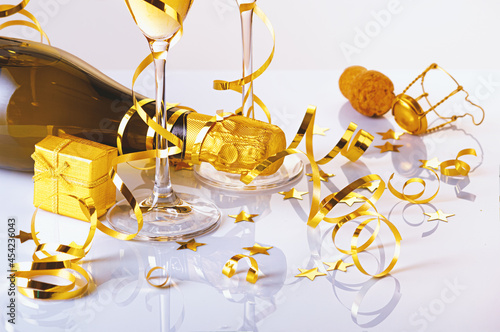 Two glasses of champagne with bottle, golden serpentine and a gift on a glossy surface. Selective focus