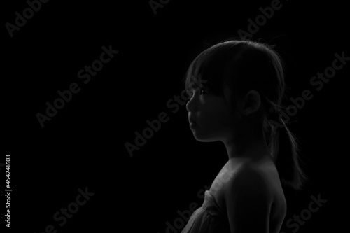 A cute adorable Asian girl about 6years old poses for a photo in the black and white background.