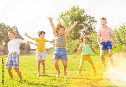 Positive kids jumping and raising hands up on green field.