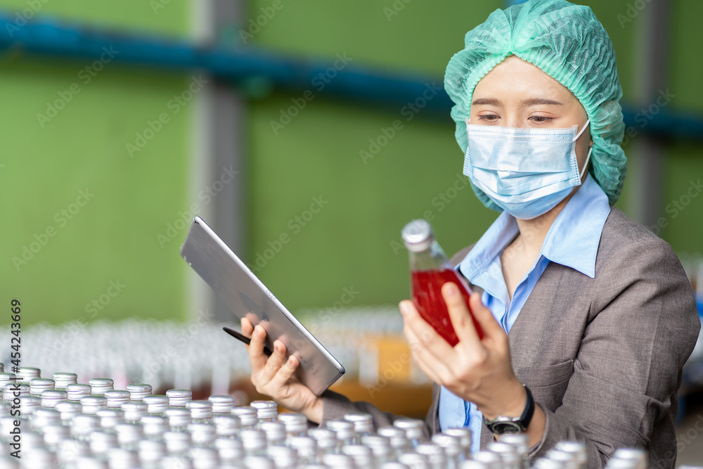 Fototapeta premium Asian female employee worker wearing mask and hairnet using digital table checking product of Basil seed with fruit in beverage factory industry. Inspection quality control
