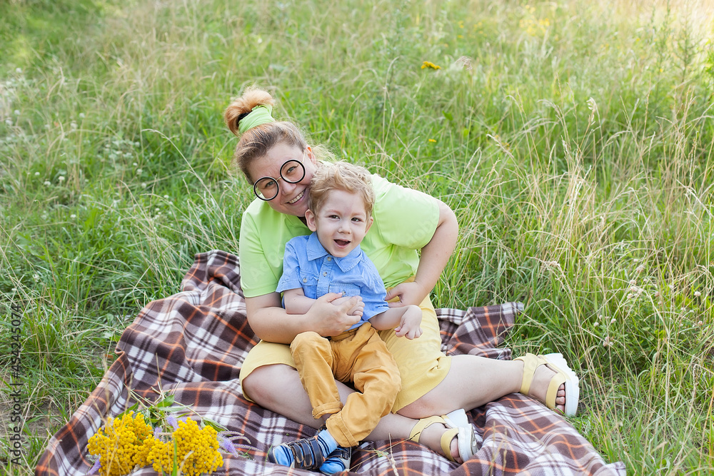 Fototapeta premium Portrait of a charming little disabled boy lying in the arms of his loving mother on the green grass in the park. disability. Mother's love. Family support.