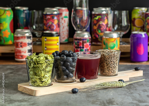 Wooden board for flight set craft beer tasting. Sour fruited blueberry IPA with ingredients. Bar with different cans in the blurred background. 