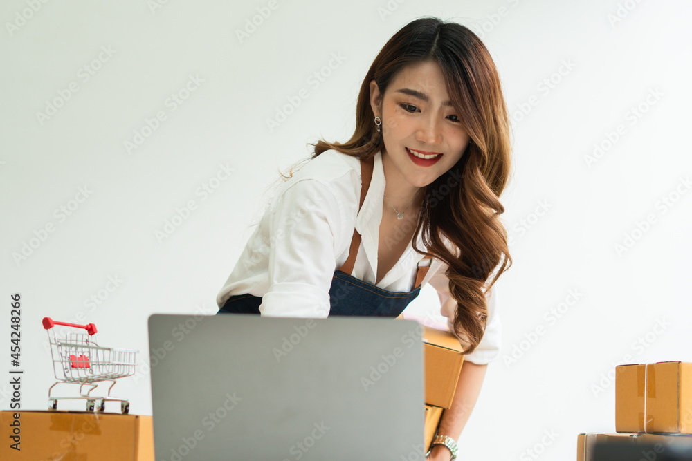 Young smiling beautiful owner asian woman freelance sme business online shopping working on laptop computer with parcel box on desk at home - SME business online and delivery concept Young smiling beautiful owner asian woman freelance sme business online shopping working on laptop computer with parcel box on desk at home - SME business online and delivery concept
