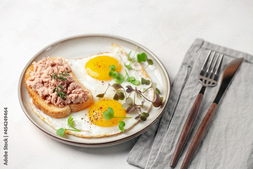 Breakfast - fried eggs and a sandwich with goose pate in a plate on the table Breakfast - fried eggs and a sandwich with goose pate in a plate on the table
