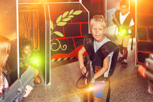 Emotional teen boy with laser pistol playing laser tag with friends on dark labyrinth. High quality photo