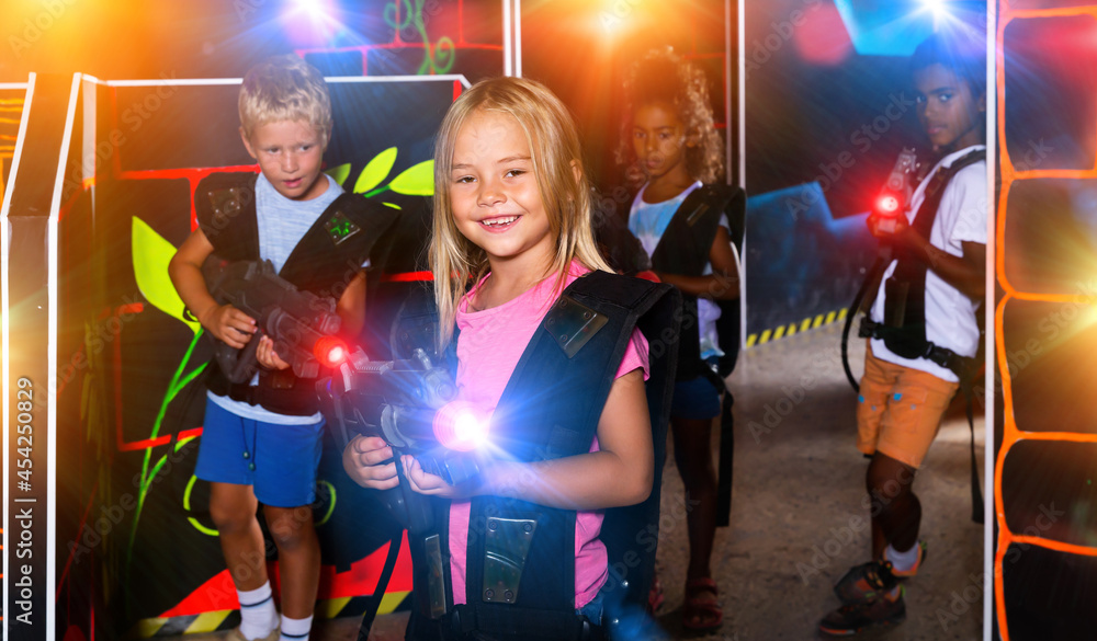 Smiling girl aiming laser gun at other players during lasertag game in dark room. High quality photo