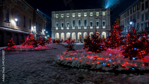 Bergamo, Italy. The main square of the old town. Landscape at the main library and buildings after a snowfall. Christmas time. Small pine trees with lights. Bergamo best of Italy