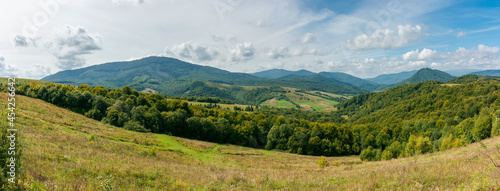carpathian countryside in september. beautiful mountain landscape with grassy field on the hill. rural scenery with village in the distant valley on a sunny day with clouds on the sky © Pellinni