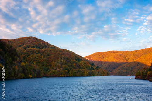 mountain lake lacul tarnita at sunrise. beautiful autumnal countryside landscape of cluj country, romania. trees on the hill in colorful foliage. clouds on the sky in morning light photo