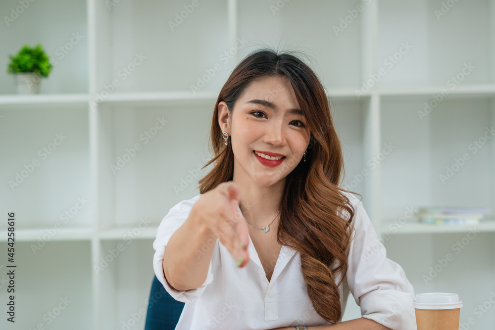 Smiling young Asian business woman extending a handshake while standing in an office Smiling young Asian business woman extending a handshake while standing in an office