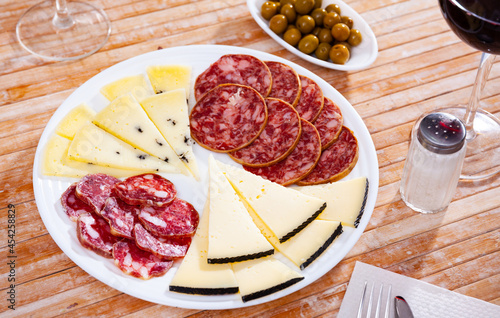 Slices of Spanish cheeses, salami and fuet sausage on plate. Traditional meat delicacies