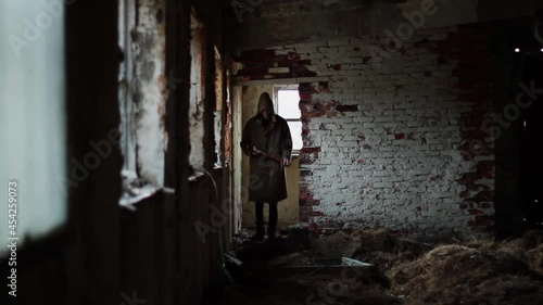 silhouette of a man in a dark cloak walking through an abandoned building with an ax. The concept for the autumn holiday halluin. photo